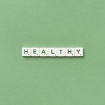 Scrabble tiles spelling the word 'healthy' on a light green background, top view.